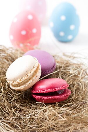 Close-up of colorful macaroons resting in straw nest and Easter eggs on light backgroundの写真素材