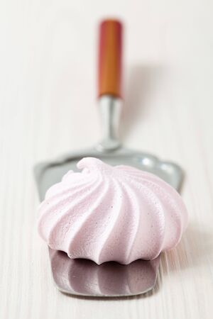 Closeup of pink meringue resting on server utensil against light backgroundの写真素材