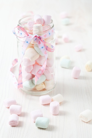 Colorful marshmallows in glass jar with ribbon on light backgroundの写真素材