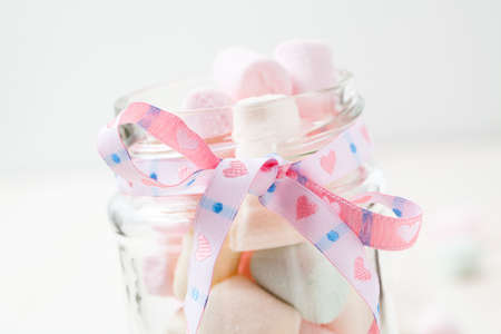 Colorful marshmallows in glass jar with ribbon on light backgroundの写真素材