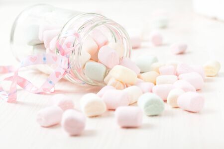 Colorful marshmallows in glass jar with ribbon on light backgroundの写真素材