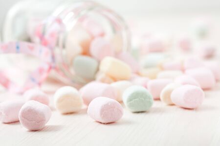 Colorful marshmallows in glass jar with ribbon on light backgroundの写真素材