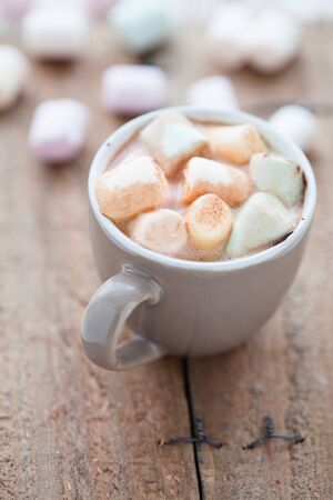 Closeup of cup of hot chocolate with coloured marshmallows resting on wooden tableの写真素材