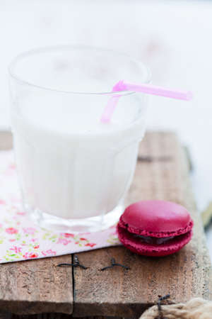Closeup of macaroon and glass of milk with pink straw on wooden tableの写真素材