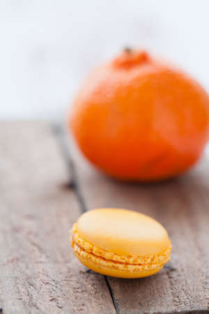 Closeup of yellow macaroon resting on wooden table with orange in backgroundの写真素材