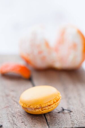 Closeup of yellow macaroon resting on wooden table with peeled orange in backgroundの写真素材