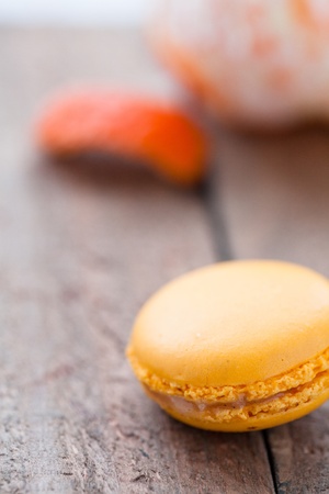 Closeup of yellow macaroon resting on wooden table with peeled orange in backgroundの写真素材