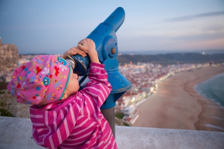 Young girl looking at Nazare Portugal with telescope from viewing areaの写真素材