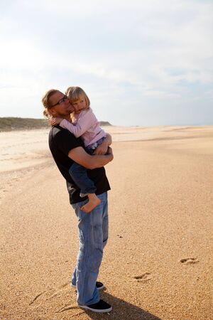 Father holding young daughter in arms at beach while on vacation in Portugalの写真素材