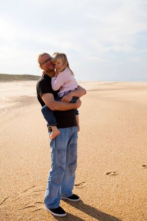 Father holding young daughter in arms at beach while on vacation in Portugalの写真素材