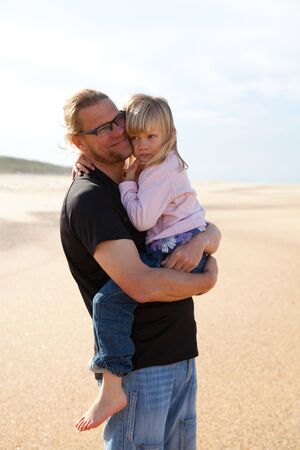 Father holding young daughter in arms at beach while on vacation in Portugalの写真素材