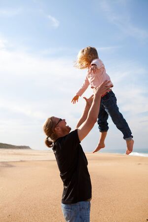 Father throwing young daughter into the air at beach while on vacationの写真素材