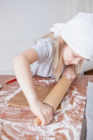 Young girl working on dough with rolling pin to make gingerbread biscuitsの写真素材