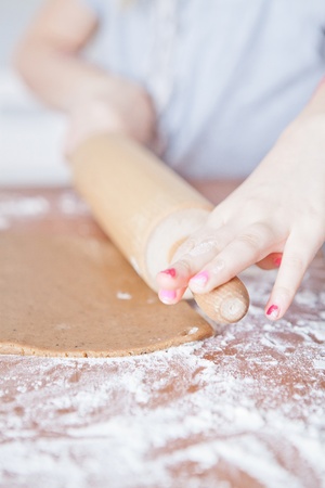 Closeup of hands of young girl and rolling pin working on dough to make gingerbread biscuitsの写真素材