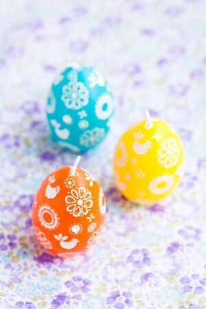 Closeup of three colorful Easter egg shaped candles on patterned surfaceの写真素材