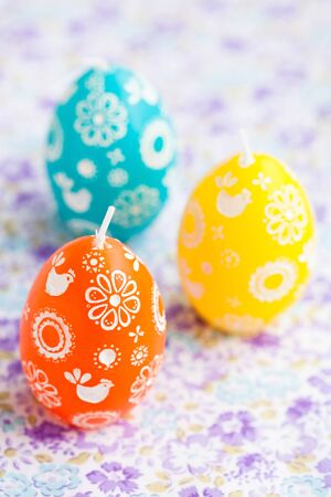 Closeup of three colorful Easter egg shaped candles on patterned surfaceの写真素材