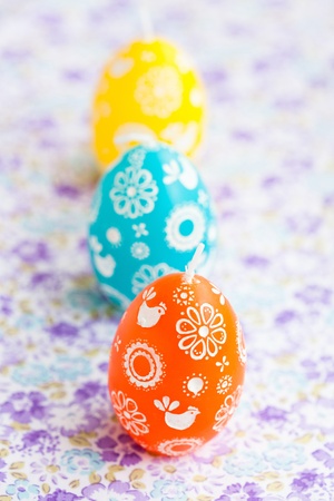 Closeup of three colorful Easter egg shaped candles in row on patterned surfaceの写真素材