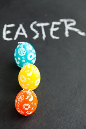 Closeup of three colorful Easter egg shaped candles and text written in chalk on dark backgroundの写真素材