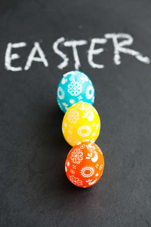 Closeup of three colorful Easter egg shaped candles and text written in chalk on dark backgroundの写真素材