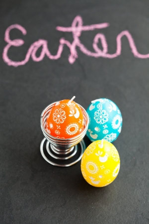 Closeup of three colorful Easter egg shaped candles with text written in pink chalkの写真素材