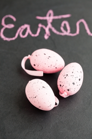 Closeup of three pink spotty Easter eggs and text written in chalk on dark surfaceの写真素材