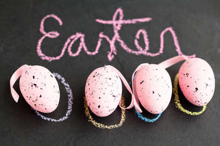 Closeup of four pink spotty Easter eggs and text written in chalk on dark surfaceの写真素材
