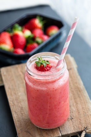 Closeup of strawberry fruit smoothie and tray of fresh strawberries in backgroundの写真素材