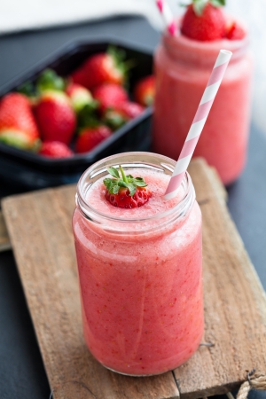 Closeup of strawberry fruit smoothies and tray of fresh strawberries in backgroundの写真素材