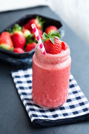 Closeup of strawberry fruit smoothie and tray of fresh strawberries in backgroundの写真素材