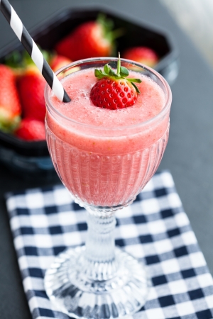 Closeup of strawberry fruit smoothie in glass with straw resting on checkered servietteの写真素材