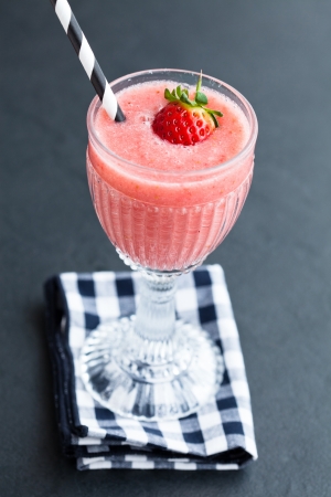 Closeup of fruit smoothie with strawberry piece in glass with straw resting on checkered napkinの写真素材