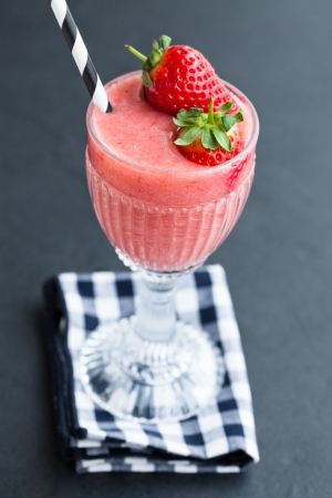 Closeup of fruit smoothie with strawberry pieces in glass resting on checkered napkinの写真素材
