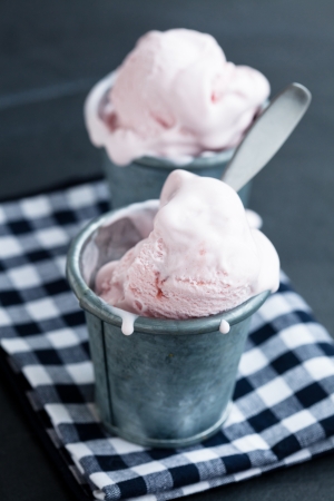 Closeup of strawberry ice cream in two metal cups on checkered serviette over dark backgroundの写真素材