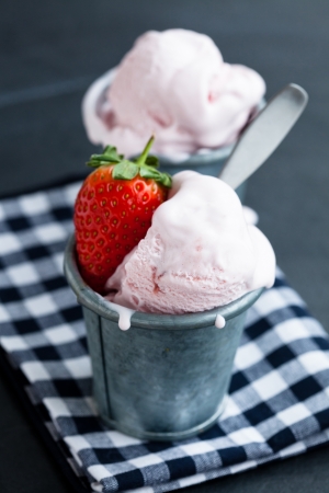 Closeup of strawberry ice cream and strawberry in two metal cups on checkered serviette over dark backgroundの写真素材