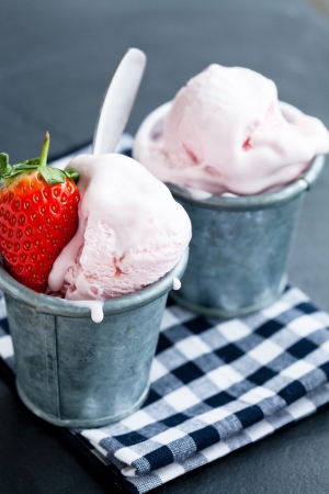 Closeup of strawberry ice cream and strawberry in two metal cups on checkered serviette over dark backgroundの写真素材