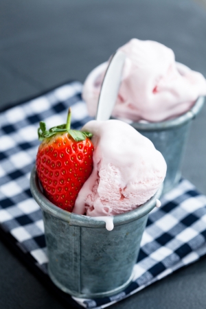 Closeup of strawberry ice cream and strawberry in two metal cups on checkered serviette over dark backgroundの写真素材