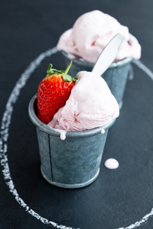 Closeup of strawberry ice cream and strawberry in two metal cups inside chalk circle on dark backgroundの写真素材