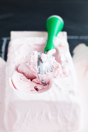 Closeup of tub of strawberry ice cream and scoop on dark backgroundの写真素材