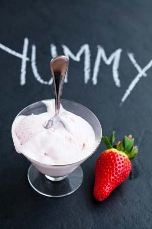 Strawberry ice cream in glass bowl and whole strawberry on dark background with text written in chalkの写真素材