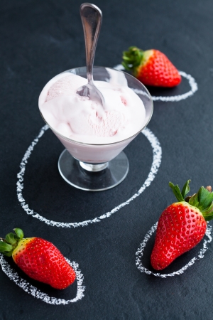 Strawberry ice cream in glass bowl and three whole strawberry on dark backgroundの写真素材