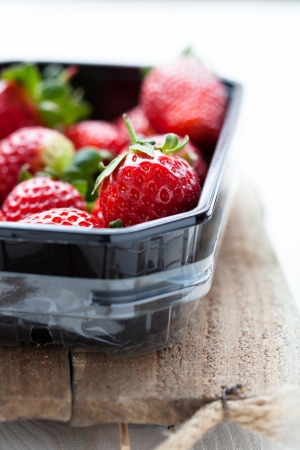 Fresh whole strawberries in plastic packing tray on wooden surfaceの写真素材