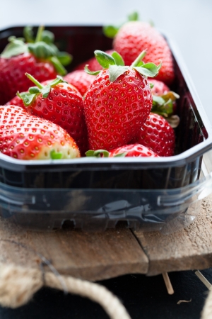 Fresh whole strawberries in plastic packing tray on wooden surfaceの写真素材
