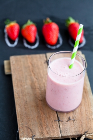 Strawberry smoothie with striped straw and whole strawberries on dark backgroundの写真素材