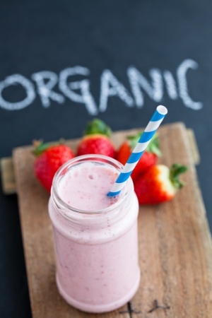 Strawberry smoothie with striped straw and whole strawberries on wooden serving trayの写真素材