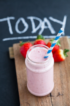 Strawberry smoothie with striped straw and whole strawberries on wooden serving trayの写真素材