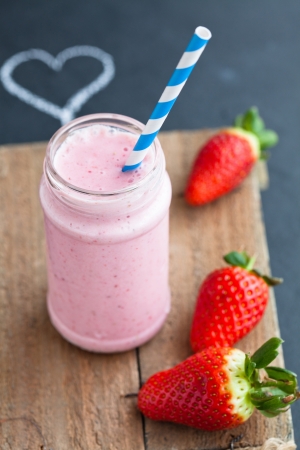 Strawberry smoothie with striped straw and whole strawberries with chalk heart drawingの写真素材
