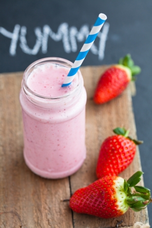 Strawberry smoothie with striped straw and whole strawberries on wooden serving trayの写真素材