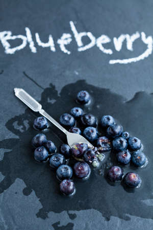 Fresh blueberries and fork and word blueberry written in chalk on dark backgroundの写真素材