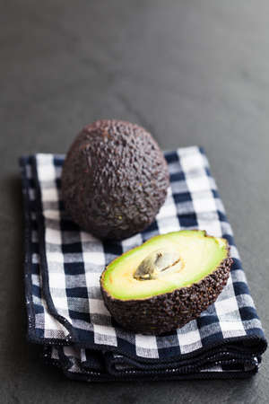 Closeup of fresh avocado halves resting on checkered napkin on dark background