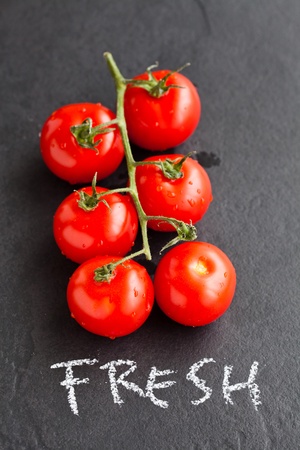 Bunch of fresh red tomatoes with word fresh written in chalk on dark backgroundの写真素材
